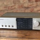 Stříbrný stereo zesilovač s černým ovládacím panelem vpravo. Na přední straně je nápis PIONEER STEREO AMPLIFIER AX5 a ovládací prvky s popisky BASS,…