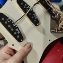 Bílá pickguard s třemi jednoduchými snímači, která je přiložena k červené elektrické kytáře. Na krytech snímačů jsou ručně napsány bílé značky: na pr…