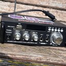 Černý audio zesilovač s ovládacím panelem. Na přední straně jsou nápisy MP3, MMC CARD, POWER, TREBLE, BASS, MIC. VOL, MIC1, MIC2 a VOLUME, dále tlačí…