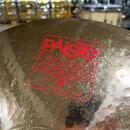 Detailní záběr na povrch kovového činele. Na povrchu je červený nápis PAiste 2002, pod kterým je logo s hvězdou a půlměsícem a text TRADE MARK MADE I…