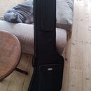 Černý poloměký pouzdro (gig bag) na kytaru. Na přední kapsi je bílé logo v oválu s nápisem "di-marzio". Povrch materiálu vypadá čistě a bez viditelné…