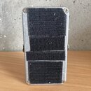 Záběr na spodní stranu efekt pedálu s kovovým, stříbrným povrchem. Na spodku je přilepený černý suchý zip, který vykazuje známky opotřebení a znečišt…