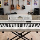 Stříbrošedý digitální klavír značky YAMAHA umístěný na černém X-stojanu. Na horním panelu je uprostřed logo YAMAHA a vpravo nápis graded Zram. Nástro…