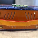 Modrá harmonika s mramorovým vzorem a oranžovými plastovými kryty. Nástroj má v horní části bílé knoflíky a uprostřed je upevněn široký oranžový popr…