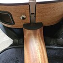 Detailní pohled na spoj hnedebního nástroje, pravděpodobně kytary, kde je krk z dřeva spojen s korpusem. Na zadní straně korpusu je vidět kovový spoj…