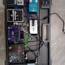 Sada kytarových efektů v černém plastovém kufru. Jsou zde pedály s nápisy: „DUNLOP CRY BABY“, „Ethereal Delay and Reverb“, „electro-harmonix ecstatic…