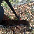 Detailní pohled na tmavě hnědé tělo elektrické kytary s vysokým leskem. Nástroj je umístěn na černém stojanu v terénu na suchém listí. Na povrchu těl…