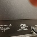 Detailní záběr na zadní část černého kytarového komba s texturovaným povrchem. Na přístroji je bílý nápis: ENGL 60 W All-tube Guitar Head Amp Firebal…