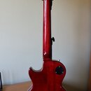 Zadní pohled na elektrickou kytaru s červeným lakovaným povrchem z dřeva. Na hlavě nástroje jsou vidět bílé ladičky a logo s nápisem "Epiphone". Na z…