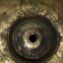 Detailní pohled do vnitřku mosazného předmětu s kruhovým otvorem uprostřed. Povrch vykazuje výrazné opotřebení, oxidaci a tmavé skvrny. Jsou vidět ko…