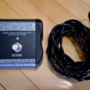 Na fotografii je stříbrný efektový pedál s černými bočními stěnami a černý kabel. Na horní ploše je logo Fender, nápis FENDER MUSICAL INSTRUMENTS COR…