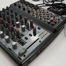 Šedý mixážní pult značky BEHRINGER s modelem XENYX 1202. Zařízení obsahuje řadu regulačních knoflíků, posuvník a kontrolní LED diody. K mixážní pultu…