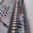 Šikmý pohled na digitální mixovací pult značky Soundcraft, model Si COMPACT. Do zadního panelu je zapojeno velké množství kabelů s konektory XLR. Pov…