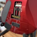 Detail zadní strany červené elektrokytary s viditelným mechanismem tremola v otvoru. Jsou zde tři pružiny a kovová základna s šesti šrouby. V dolní č…