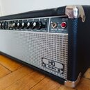 Kytarový kombozesilovač v černém vinylovém potahu s kovovými rohy a stříbrnou textilní maskou reproduktoru. Na ovládacím panelu je nápis MUSIC MAN IN…