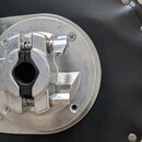 Detailní pohled na kovový mechanismus s upínací hlavou, který je připevněn k černé koženkové ploše. Kovový povrch vykazuje drobné škrábance a známky…