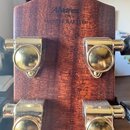 Záběr na zadní stranu hlavy akustické kytary z hnědého dřeva. V horní části je vyryt logo Alvarez a pod ním nápis HAND CRAFTED. Na hlave jsou vidět č…
