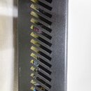 Detailní pohled na černý kovový šasi s řadou šikmých ventilačních otvorů. Prostředu otvory jsou vidět vnitřní elektronické součástky, konkrétně konde…