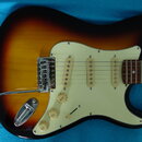 Elektrická kytara s trupem v barevnosti sunburst a krčkem z tmavého dřeva. Nástroj má tři snímače typu single-coil, bílý pickguard a tři ovládací kno…