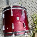 Červený buben s kovovými obručemi a lugy. Povrch je v několika místech poškrábaný a jsou na něm vidět zbytky nalepených nálepek. Na nástroji nejsou ž…