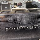 Černý kytarový zesilovač s texturovaným povrchem a kovovou rukojetí. Na zadním panelu je nápis MESA ENGINEERING VACUUM TUBE AMPLIFIER a řada ovládací…