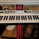 Bílá klávesová syntezátor s černými klávesami. Na levé straně je nápis YAMAHA a na pravé straně označení MX49. Horní panel obsahuje ovládací knofíky,…