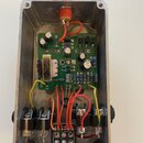 Fotografie zachycuje vnitřek efekt pedálu v hliníkovém šasi. Uvnitř je zelená základní deska s elektronickými součástkami, na které je nápis OCTAVE a…