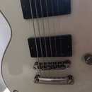 Detail bílé elektrické kytary se dvěma černými humbuckery. Na spodním snímači je viditelný nápis EMG. V dolní části těla je částečně viditelný černý…