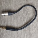 Černý audio kabel s konektory na obou koncích. Na jedné straně je stříbrný vícepinový konektor (XLR) s černým plastovým krytem, na druhé straně pozla…