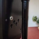 Detailní záběr na černý plastový panel s jedním zapojeným jack konektorem a čtyřmi prázdnými otvory pro další konektory. Panel je přišroubován čtyřmi…