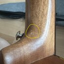 Detailní pohled na hnedý dřevěný krk hudebního nástroje s kovým ladicím kolíkem. V žlutém kruhu je zvýrazněna drobná světlá skvrna nebo oděr na povrc…