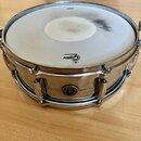 Stříbrný kovový buben s bílým membránou, na které je vidět značné opotřebení a šmouhy v centru. Na membráně je černý nápis „Gretsch FERMATONE“. Na bo…