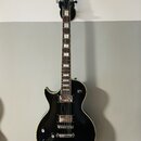 Černá elektrická kytara s tvarem singlecut a krémovým lemováním. Na hlavě je bílý nápis Bach. Nástroj má dva humbuckery, čtyři ovládací knofíky a stр…