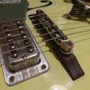 Detail elektrické kytary v žluté barvě. Na snímači je vidět nápis GRETSCH a na mostku jsou viditelné známky opotřebení a koroze. Kytara má kovový sní…