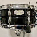 Černý buben s chromovaným obručováním a mechanismy. Na korpusu je oválný štítek s nápisy CONCERT, YAMAHA a JAPAN. Povrch nástroje je glossy, v odrazu…