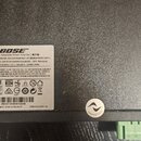 Fotografie zachycuje zadní část černého elektronického zařízení s bílým informačním štítkem. Na štítku je logo BOSE a nápis PowerShareX Adaptable Pow…