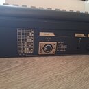 Detail zadní strany černého hudebního zařízení s několika konektory. U jednoho z nich je nápis dmx a in/out, vedle kterého je tabulka pin out: 1 = gn…