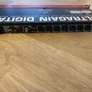 Černý rackový audio interface s červeným horním panelem. Na přední straně je nápis behringer ULTRAGAIN DIGITAL MODEL ADA8200 a řada osmi XLR konektor…