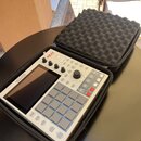 Světle šedý sampler Akai MPC One v černém přepravním pouzdře s pěnovou výplní. Na zařízení je vidět červené logo AKAI PROFESSIONAL a nápis MPC ONE. P…