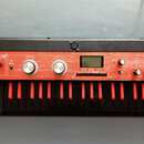 Červený syntetizátor s černou klaviaturou a černým vnějším rámem. Na horním panelu je nápis KORG microKORG X. Přístroj obsahuje displej, několik ovlá…
