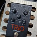 Černý efekt pedál s nápisem TRIO Band Creator. Zařízení obsahuje několik ovládacích prvků: otočný přepínač GENRE s označením ALT ROCK, ROCK, COUNTRY,…