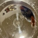 Detailní pohled na vnitřek kovového nástroje stříbrné barvy s koncentrickými rýhami na povrchu. Uprostřed se nachází kulatý otvor. Povrch vykazuje če…