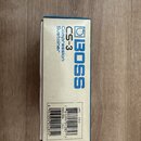 Fotografie znázorňuje papírovou krabici od efekt pedálu. Na bílém podkladu je modrý nápis BOSS, označení modelu CS-3 a text Compression Sustainer. Ve…