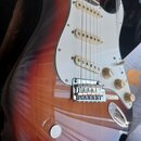 Elektrická kytara s trupem v červeno-žlutém sunburst provedení a bílým pickguardem. Nástroj má tři jednosnívací snímače s krémovými kryty, tři ovláda…