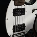 Detail elektrické kytary s černým korpusem a bílým pickguardem. Nástroj má dva černé humbuckery s viditelnými póly a chromovaný kobylník. Hmatník je…