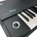 Černý klávesový nástroj s bílými a černými klávesami. Na horním panelu jsou bílé nápisy KORG a MUSIC WORKSTATION m50. V levé části je umístěn kulatý…