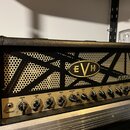 Černý kytarový zesilovač v koženém potahu s kovovou mřížkou. Na přední mřížce je umístěno oválné logo EVH a nápis 5150. Spodní ovládací panel je zlat…