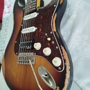 Elektrická kytara s trupem v barevném přechodu od žluté přes hnědou k černé. Nástroj má tmavě červený želvový pickguard a tři bílé snímače. Povrch la…