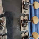 Detail zadní strany hlavy kytary s třemi ladicími mechanismy a krémovými knoflíky. Na tmavém povrchu je svisle vyrazeno sériové číslo 203831. Kovové…