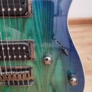 Detail korpusu elektrické kytary s modro-zeleným přechodem barev a viditnou strukturou dřeva. Nástroj má dva humbuckery s chromovanými rámečky, chrom…